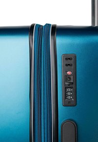 Maleta rígida con ruedas en azul metálico, que presenta un cierre con cremallera, cerradura de combinación incorporada y un diseño elegante con acentos en negro.