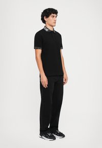 Sort polo shirt med et mønstret krave, korte ærmer med mønstrede manchetter, parret med sorte bukser og sorte sportssko.