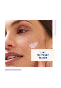 Gesichtscreme auf die Wange aufgetragen, glatte weiße Textur, zarte Haut, natürliches Makeup, helle Töne; Textüberlagerung lautet "ZART PFLEGEND TEXTUR."