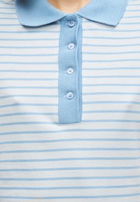 Ανοιχτό μπλε και λευκό ριγέ πόλο μπλουζάκι με γιακά, διαθέτει πέντε κουμπιά και απαλό βαμβακερό ύφασμα.