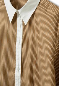 Chemise à rayures verticales marron et blanches avec col blanc et patte de boutonnage blanche à l'avant, vue en gros plan.