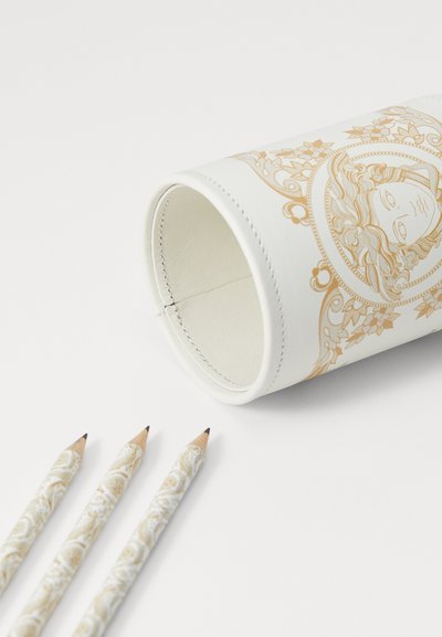 White cylindrical pencil holder with gold intricate designs and stitching. Three decorative pencils with patterned barrels beside it.