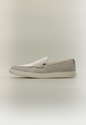Vue latérale d'une chaussure décontractée beige clair à enfiler, avec une semelle en caoutchouc et une tige en tissu sur un fond neutre.