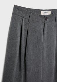 Graue plissierte Hosen mit einem Bund, der einen Knopfverschluss hat. Hergestellt aus strukturiertem Stoff, hervorgehoben durch ordentlich genähte Nähte.