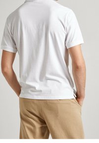 Biała bawełniana koszulka z krótkim rękawem o prostym kroju, zestawiona z beżowymi spodniami, z widocznym gładkim tyłem.