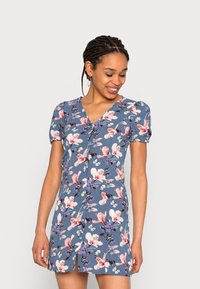 Vestido de mangas curtas em tecido azul com um padrão floral, apresentando flores rosa e brancas e borboletas, decote em V e detalhe de cintura ajustada.