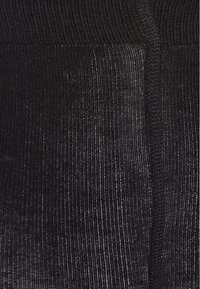 Gros plan d'un tissu tricoté noir côtelé montrant une texture verticale et des détails de couture.