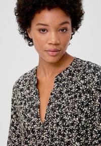 Schwarz-weiße Bluse mit floralem Muster und V-Ausschnitt, aus weichem Stoff und mit Dreiviertelärmeln. Verfügt über aufwändige Details.