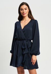 Mornarji modra obleka z ovitkom z dolgimi naborki, V-izrezom in trakastim pasom. Ima plastičen, nabrano rob in gladko teksturo.