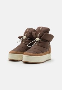 Botas de invierno acolchadas en marrón con suelas de plataforma beige y cierres de cordón elástico blanco, mostradas sobre un fondo blanco.