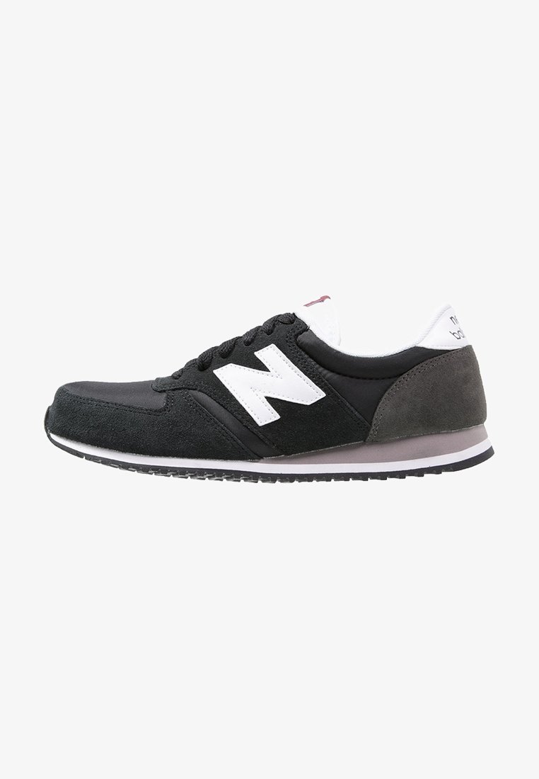 Chaussures de sport noires et grises avec une tige en suède et matériaux synthétiques, arborant un logo "N" blanc, des lacets noirs et une semelle en caoutchouc texturée.