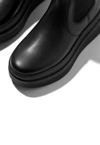 Black leather ankle boots with a smooth finish, rounded toe, elastic side panels, and a thick rubber sole. Subtle stitching details.