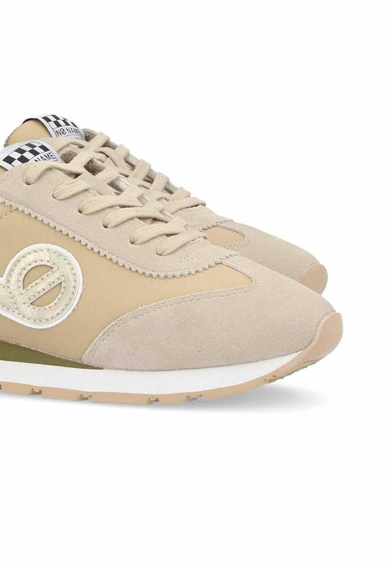 Baskets en daim beige avec des accents marron, logo rond et semelle en caoutchouc blanc. Présente un design à lacets et une étiquette à carreaux sur la languette.