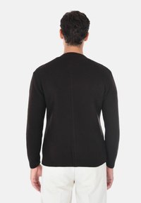 Maglione nero a maglia con maniche lunghe, design testurizzato e cucitura centrale dritta, abbinato a pantaloni di colore chiaro.