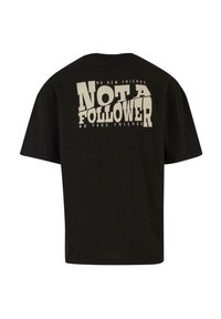 Sort bomulds T-shirt med korte ærmer, der har en iøjnefaldende, cremefarvet grafisk tekst på ryggen: "IKKE EN FØLGER" med yderligere sætninger over og under.