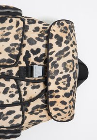 Plecak w panterkę z teksturowanej tkaniny, czarne akcenty, zamknięcie na górny zamek oraz metalowa klamra z przodu.