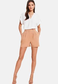 Blusa bianca a maniche corte con scollo a V abbinata a pantaloni corti plissettati beige. Presenta tasche laterali e vita aderente.