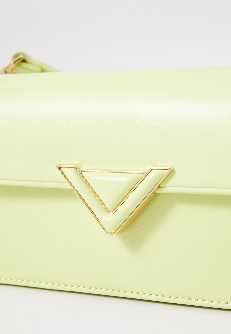 Sac en simili cuir vert clair avec une texture lisse, présentant un accent matériel triangulaire doré et des détails cousus le long des bords.