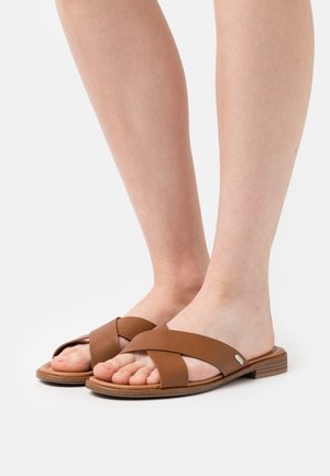 Sandales en cuir marron avec des brides croisées, semelles plates et finition texturée. Semelle intérieure légèrement rembourrée, affichant la forme naturelle du pied.