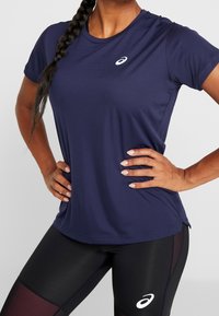 Maglietta sportiva blu navy a maniche corte, in tessuto leggero e strutturato, con piccolo logo bianco sul petto. Abbinata a leggings neri.