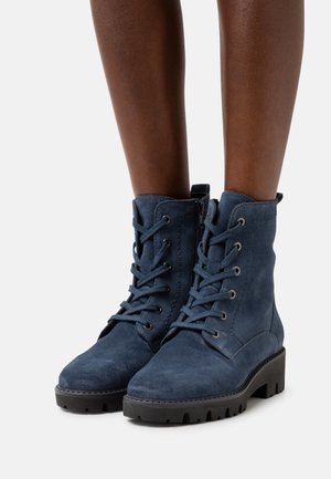 Botines de ante azul con puntera redondeada, cordones en la parte frontal y cremallera lateral. Suela de goma negra gruesa con patrón antideslizante.