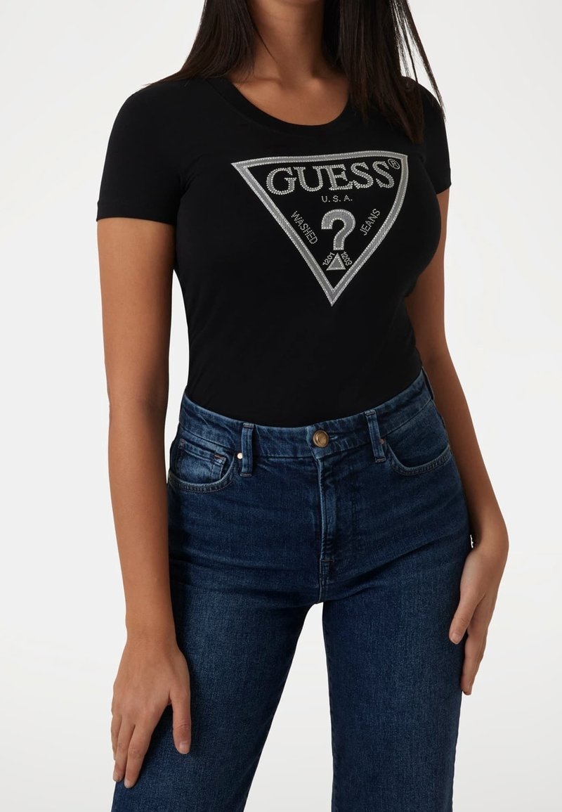 Sort t-shirt med korte ærmer, der har et sølv trekantlogo design. Kombineret med mørkeblå højtaljede jeans.