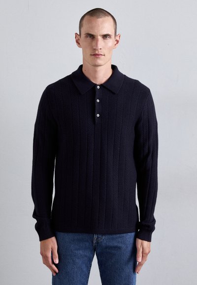 Pulover tricotat bleumarin cu textură structurat, având un guler clasic și închidere cu trei butoane, asortat cu blugi din denim.