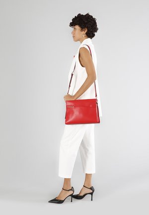 Rode leren crossbody tas met een strak ontwerp, verstelbare schouderriem en een ritsvak. Soepele textuur met een reliëflogo detail.