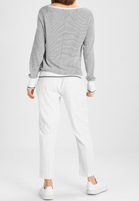 Szary sweter w paski z prążkowanymi mankietami, zestawiony z białymi spodniami w delikatny prążek, o dopasowanym kroju i gładkiej fakturze. Uzupełniony białymi sneakersami.