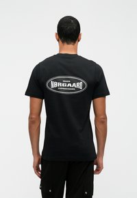 Schwarzes Baumwoll-T-Shirt mit einem weißen Grafikdruck auf dem Rücken, der den Text "MADS NØRGAARD KOPENHAGEN" in einer ovalen Form zeigt.