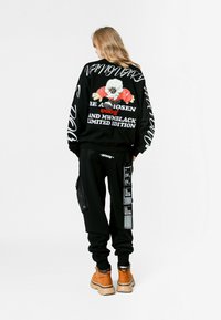 Sudadera negra de gran tamaño con texto y gráfico en blanco; combinada con pantalones deportivos negros con bolsillo tipo cargo y diseño de etiqueta. Botas beige.