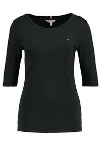Černý top s dlouhým rukávem vyrobený z jemného materiálu. Má široký výstřih a malou logotypovou značku na hrudi. Jednoduchý design bez vzorů.