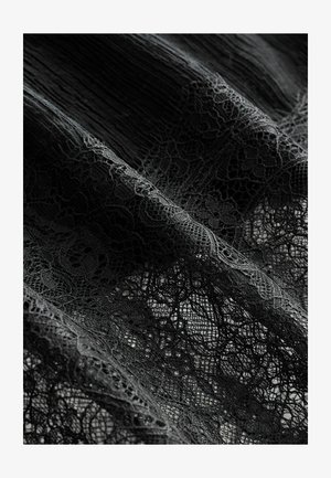Czarna koronkowa tkanina z misternymi wzorami kwiatowymi, z fakturowaną powierzchnią i drobnymi detalami, nałożona na gładkie tło.
