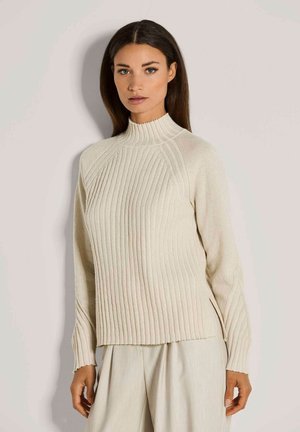Cremfarbener Strickpullover mit geripptem Muster, hohem Kragen und seitlichen Schlitzen. Lange Ärmel mit dezenten Details entlang der Nähte.