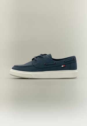 Scarpe in pelle blu navy con suola in gomma bianca, caratterizzate da lacci rotondi, cuciture decorative e una piccola etichetta con il logo sul lato.