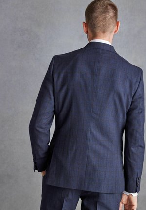 Traje de cuadros azul oscuro con un corte estructurado. Presenta solapas de muesca, dos botones y una textura suave. Vista trasera con pantalones a medida.