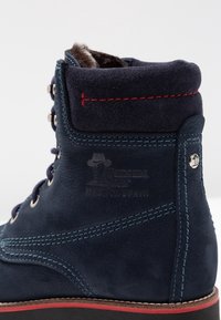 Marinblå Panama Jack-stövlar med röd sömnad, vadderad krage, metallöglor, pälsfoder och präglad "Made in Spain"-logga på sidan.