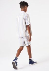 Korte mouwen gestreepte shirt en bijpassende shorts in beige met lichtblauwe en witte strepen, gemaakt van lichtgewicht stof. Witte hoge sneakers.
