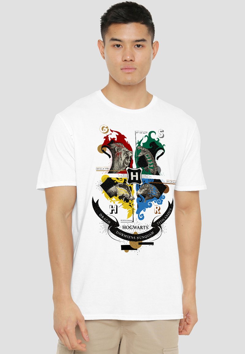 Man wearing white t-shirt with colorful Hogwarts crest featuring lion, snake, badger, and eagle mascots and Latin motto banner.