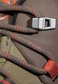 Bruine wandelschoen met donkergroene stof, voorzien van gevlochten veters met rode accenten en een metalen grijze sluiting met het label "MAMMUT."
