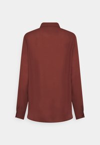 Chemise bordeaux à manches longues avec un col classique, une texture lisse et un ourlet arrondi. Elle présente des poignets boutonnés et une silhouette fluide.