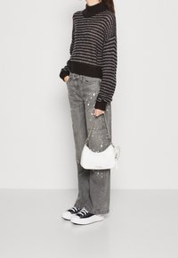 Maglione a righe bianche e nere, pantaloni cargo grigi con design splatter, borsa bianca con tracolla a catena e sneaker nere.