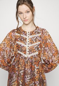 Vestido floral de manga longa com um padrão castanho, laranja e roxo, decote redondo, fecho de botão e detalhes em renda no corpete.