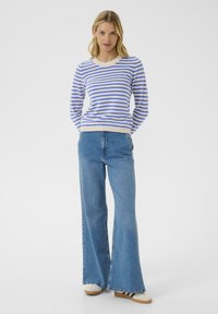 Blue and white striped sweater with a ribbed neckline, paired with light blue flared jeans, and white shoes with black accents.