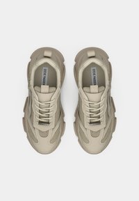 Beige Sport Schuhe mit einer strukturierten Oberseite und Mesh-Einsätzen, runden Schnürsenkeln und verstärkten Fersenschlaufen für zusätzlichen Halt, die ein modernes Design zeigen.