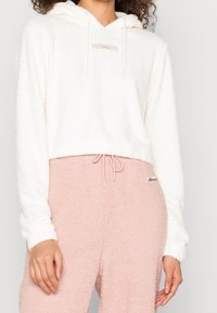 Witte, fuzzy cropped hoodie met een trekkoord en een klein logo. Gecombineerd met roze, gestructureerde joggers met een elastische tailleband.