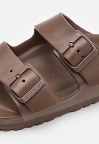 Brune Birkenstock-sandaler med to justerbare stropper, spenner og en teksturert såle. Laget av mykt, slitesterkt materiale med en polstret såle.