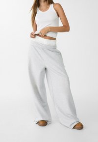 Lichtgrijze sweatpants met een elastische tailleband, een relaxte pasvorm en een zachte textuur. Gestapeld bij de enkels, gecombineerd met bruine schoenen.