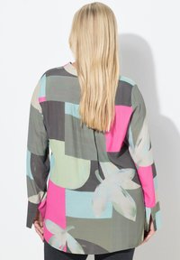 Langærmet skjorte med et flerfarvet mønstret stof i nuancer af grå, pink, grøn og blå med blomster- og abstrakte former.