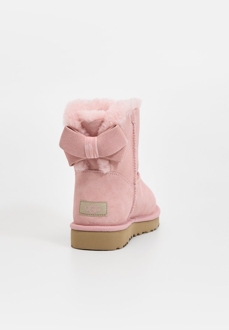 Rosa Wildleder-Ankle-Boot mit weichem Kunstfellfutter, einem dekorativen Bogen auf der Rückseite und einer Gummisohle. Mit einem aufgenähten Logo-Patch an der Seite.